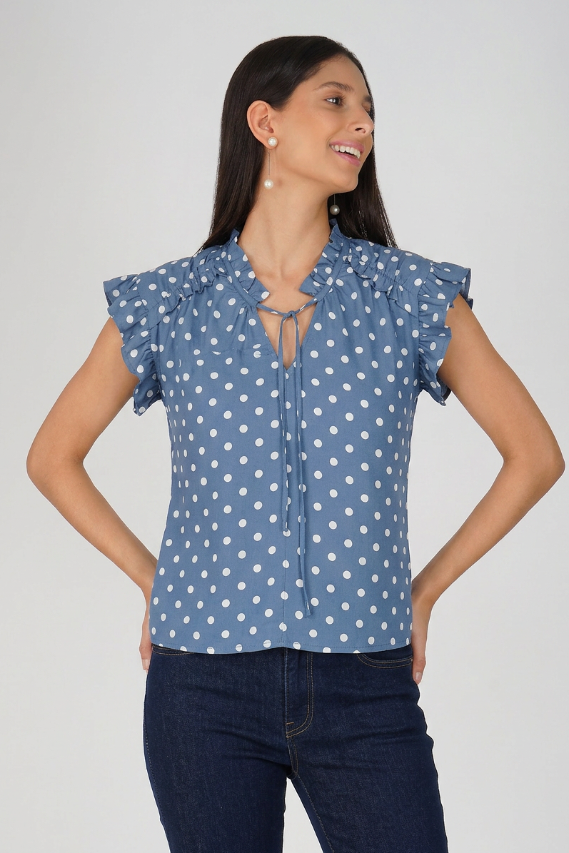Woman wearing a blue polka dot blouse with ruffled sleeves on a plain background