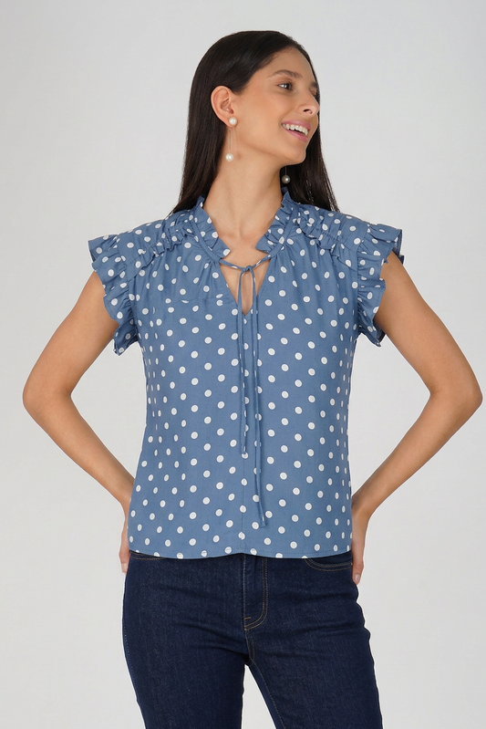 Woman wearing a blue polka dot blouse with ruffled sleeves on a plain background